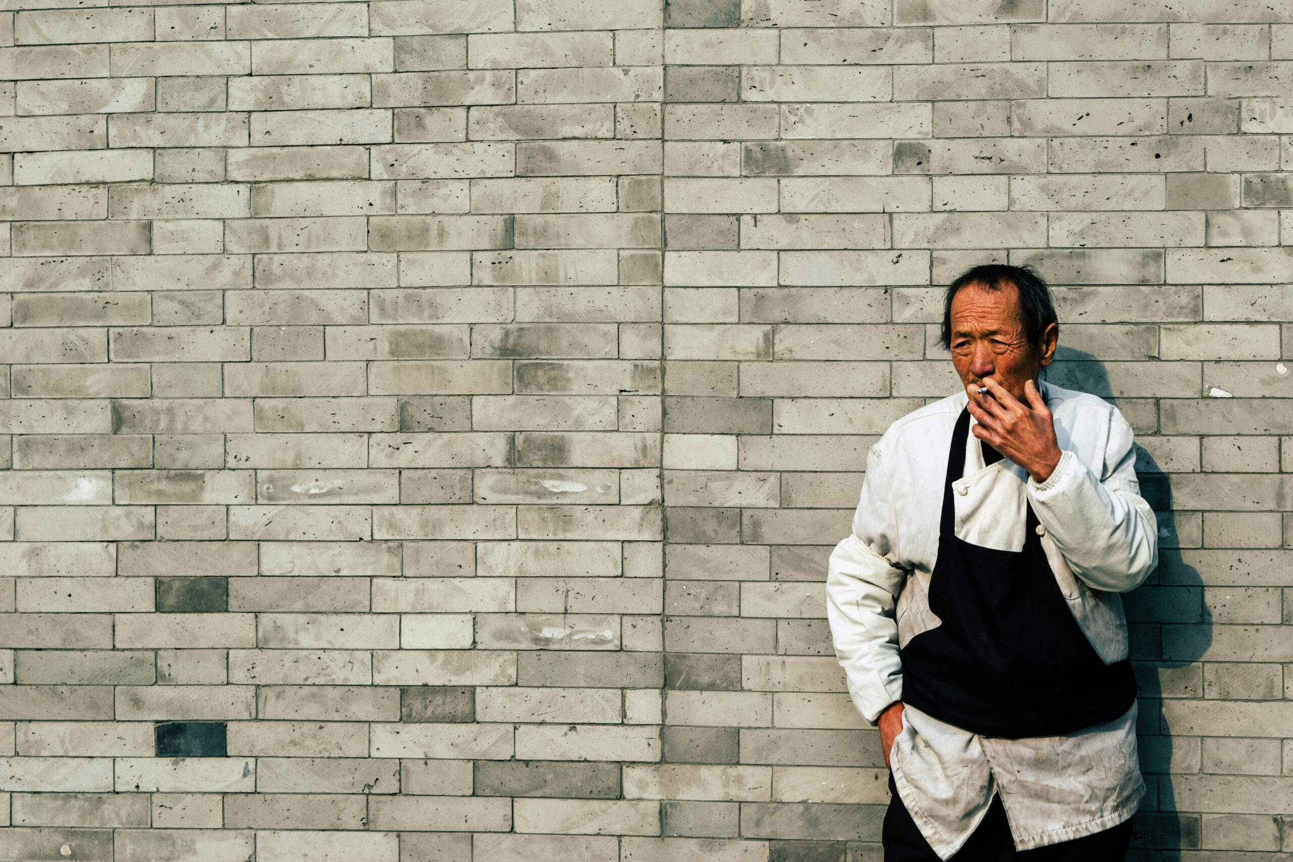 man in white dress shirt leaning on gray brick wall